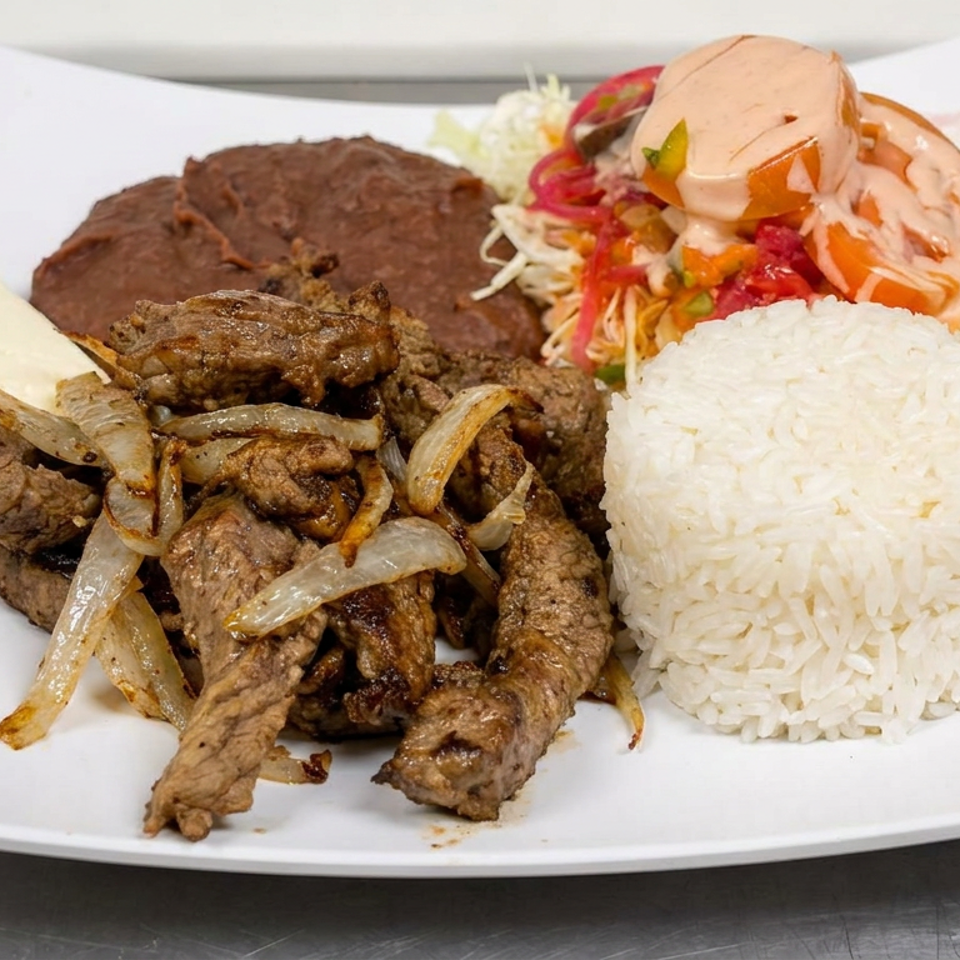 Plate of grilled beef with onions, white rice, beans, cheese, and colorful salad topped with creamy sauce.